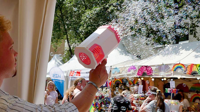 Ein Mitarbeiter der Immanuel Albertinen Diakonie sprüht mit einer Seifenblasenkanone in der Hand zahlreiche Seifenblasen in die Luft beim lesbisch-schwulen Stadtfest Motzstraßenfest rund um den Nollendorfplatz in Berlin-Schöneberg.